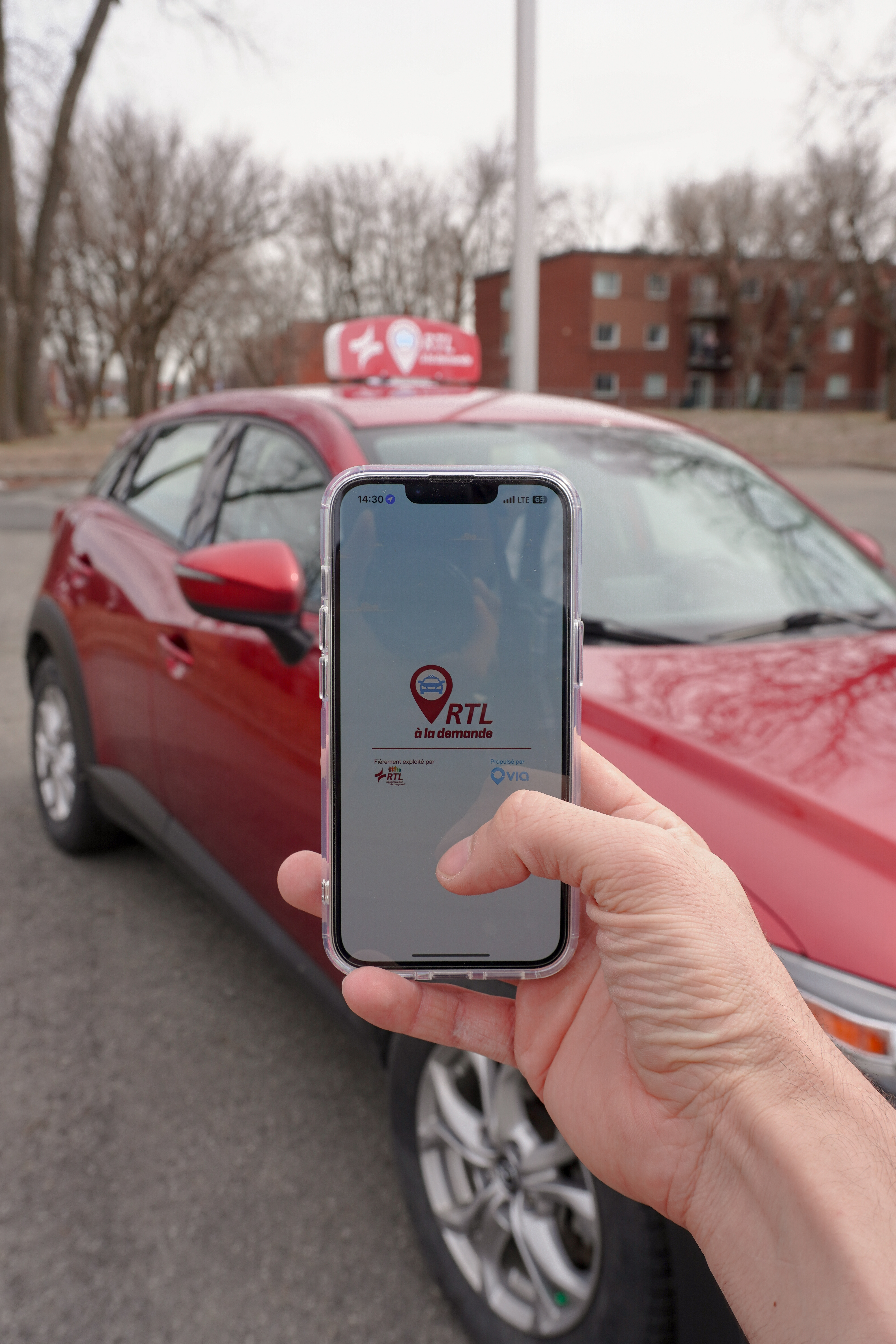 Un téléphone affichant l’application RTL à la demande, avec le véhicule qui arrive en arrière-plan